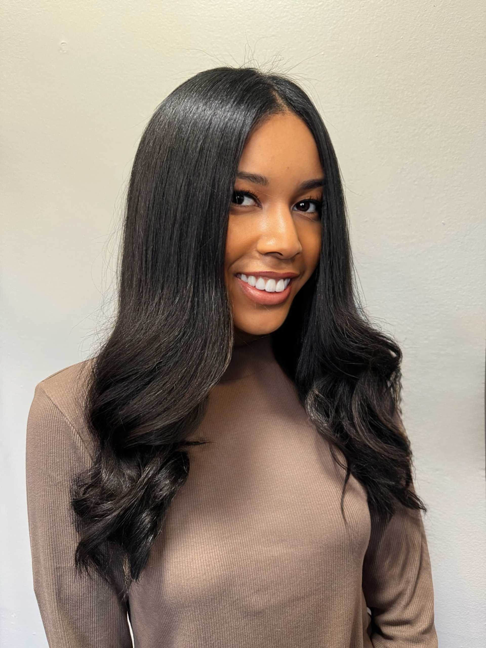 Young woman with long, straight black hair smiling against a plain background.
