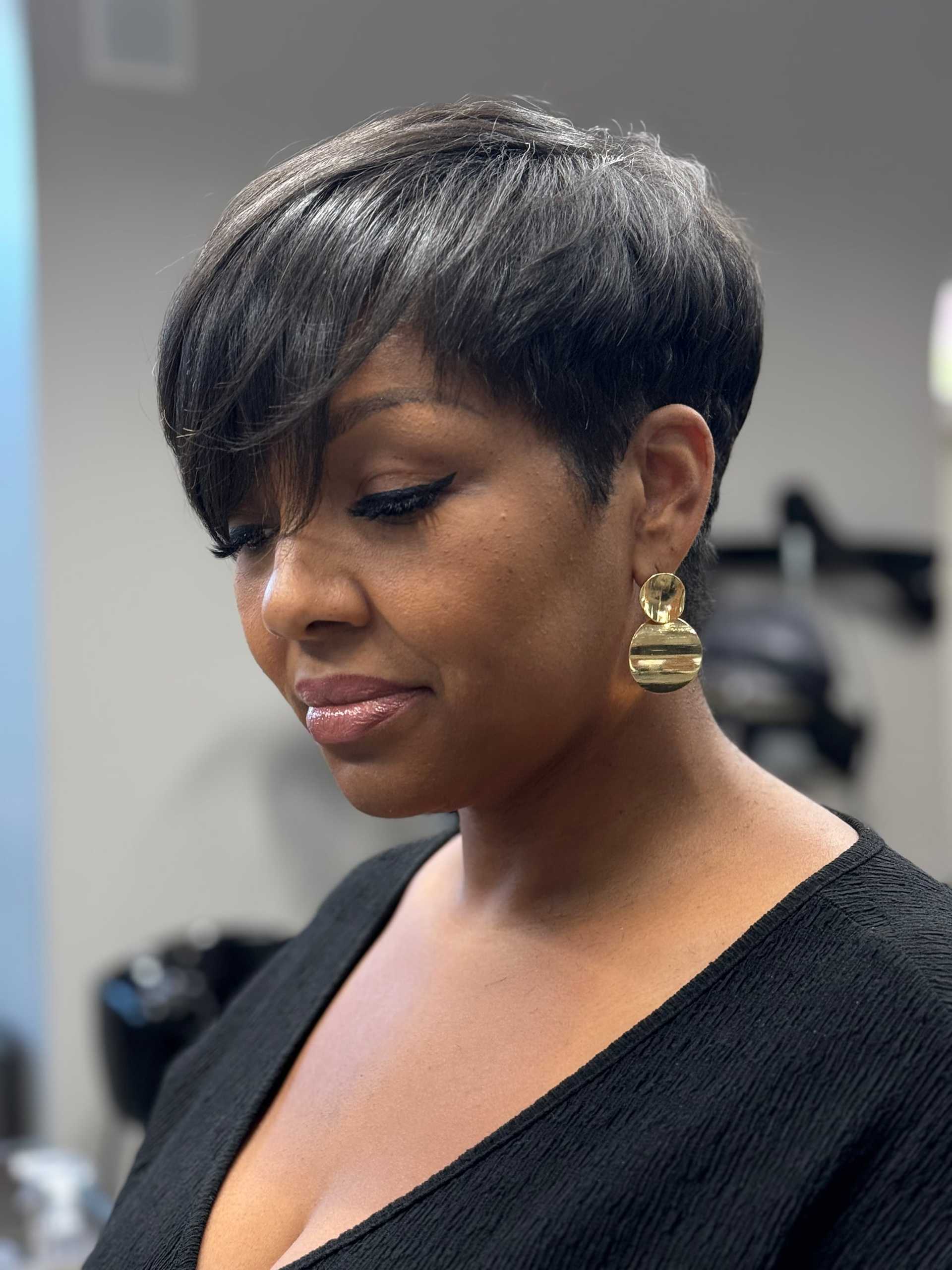 Woman with short hair, gold earrings, and black top in a modern setting.