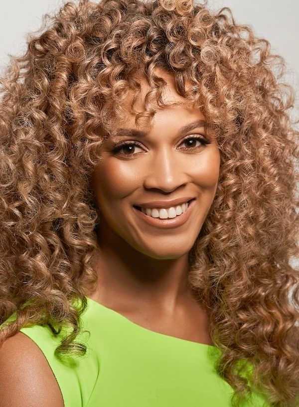 Smiling person with curly hair wearing a bright green top.